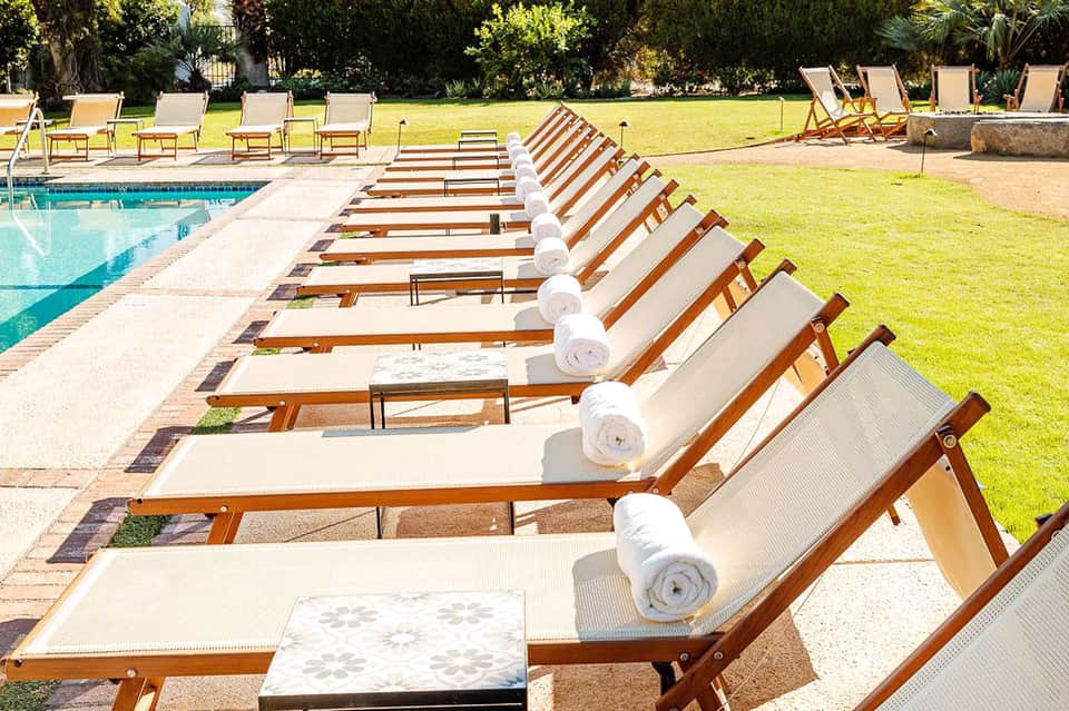 Row of wooden lounge chairs with white towels by a rectangular pool and manicured lawn