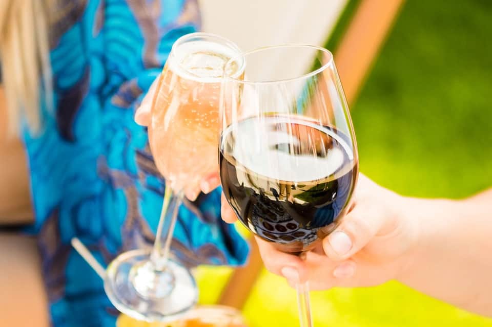 Two glasses of wine held by hands outdoors with blurred blue background