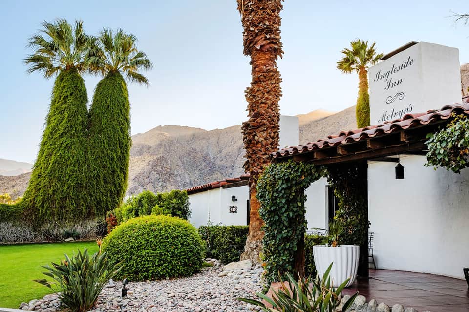 Spanish colonial-style inn with white walls, palm trees, manicured gardens, and mountain backdrop