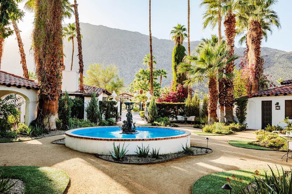 Round blue fountain in desert courtyard surrounded by white Spanish-style buildings and tall palm trees