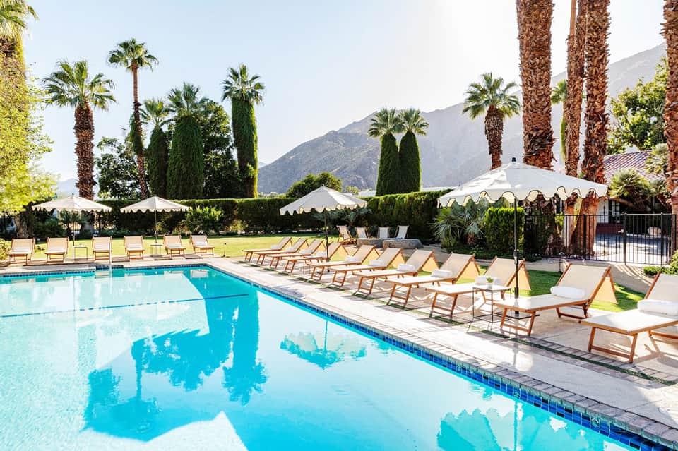 Luxury resort pool with mountain backdrop, lounge chairs, and palm trees