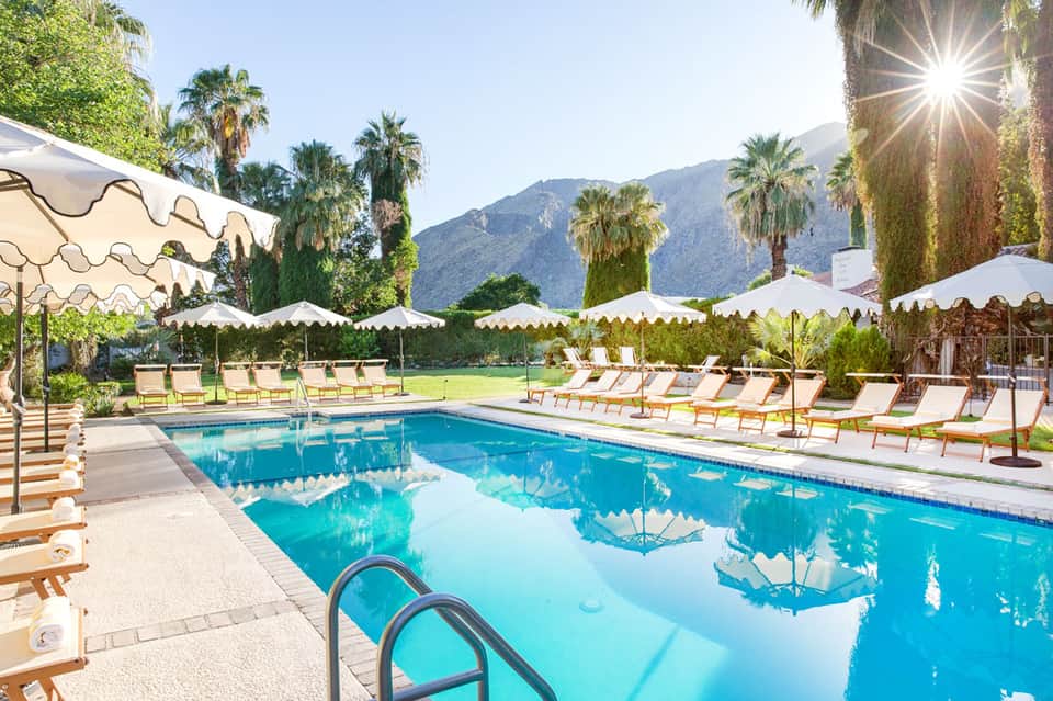 Resort pool with cream umbrellas, palm trees, and mountain backdrop