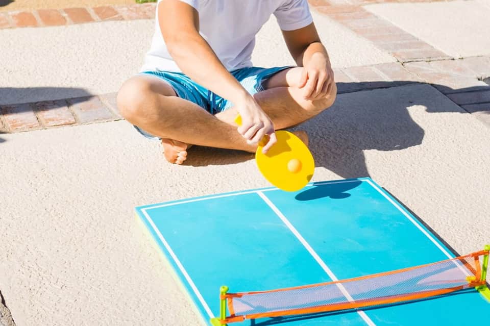 Child playing cornhole with yellow bean bag over blue board on concrete patio