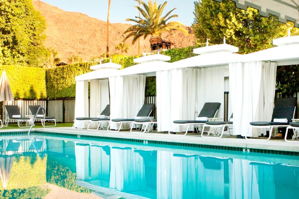 Desert resort pool with white cabanas, lounge seating, turquoise water, and mountain backdrop