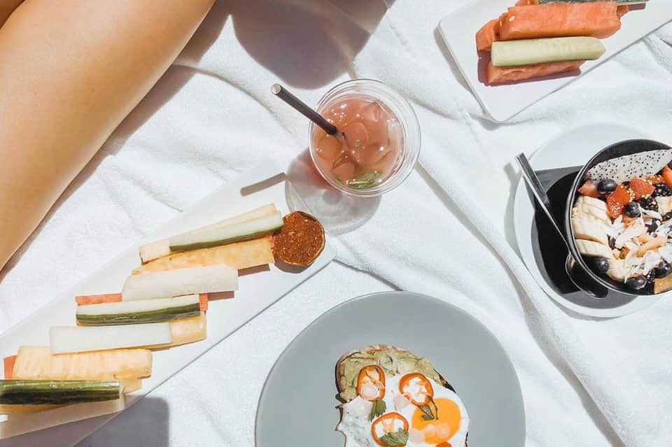 Overhead view of gourmet meal with cocktail, appetizers, and fresh vegetables on white surface