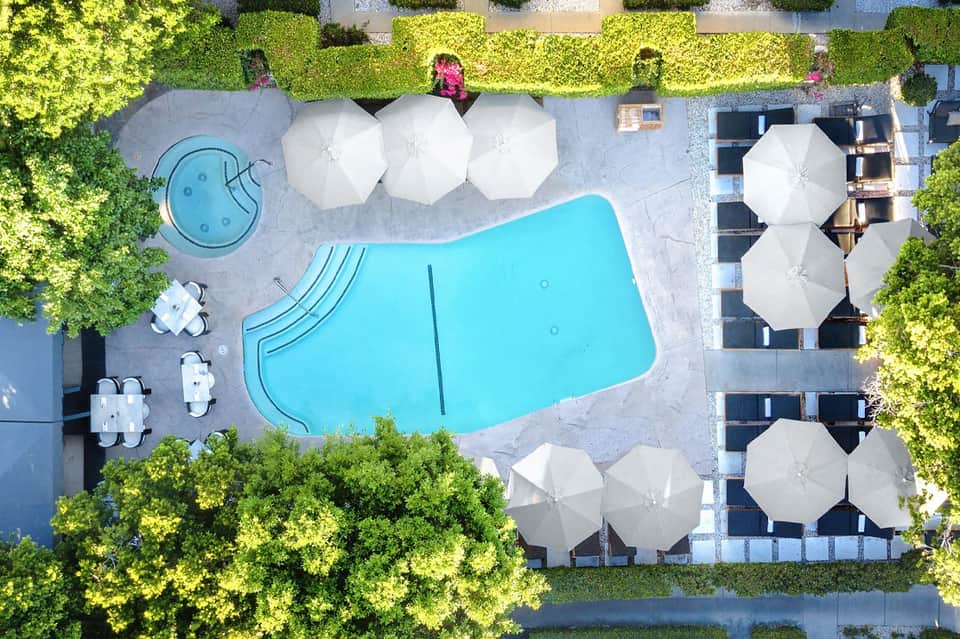 Overhead view of resort pool surrounded by white umbrellas, landscaping, and modern buildings