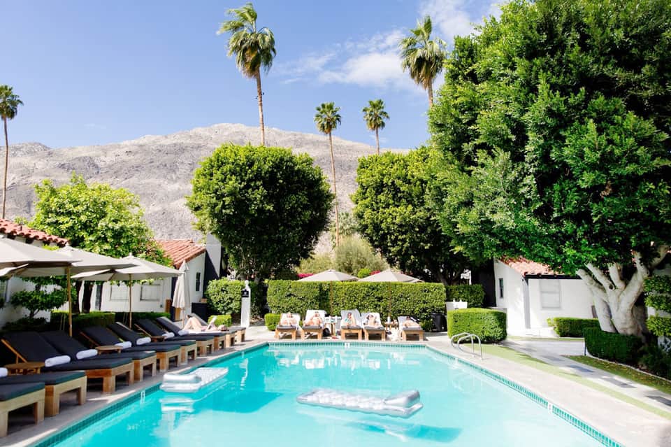 Resort pool with turquoise water, lounge chairs, palm trees, and mountain backdrop
