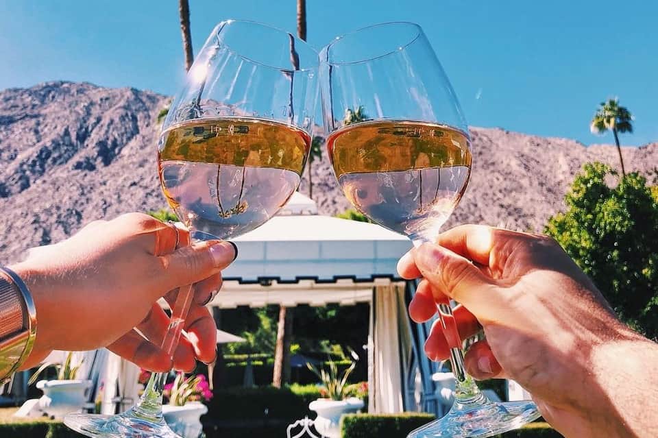 Two hands toasting with white wine glasses overlooking desert mountains