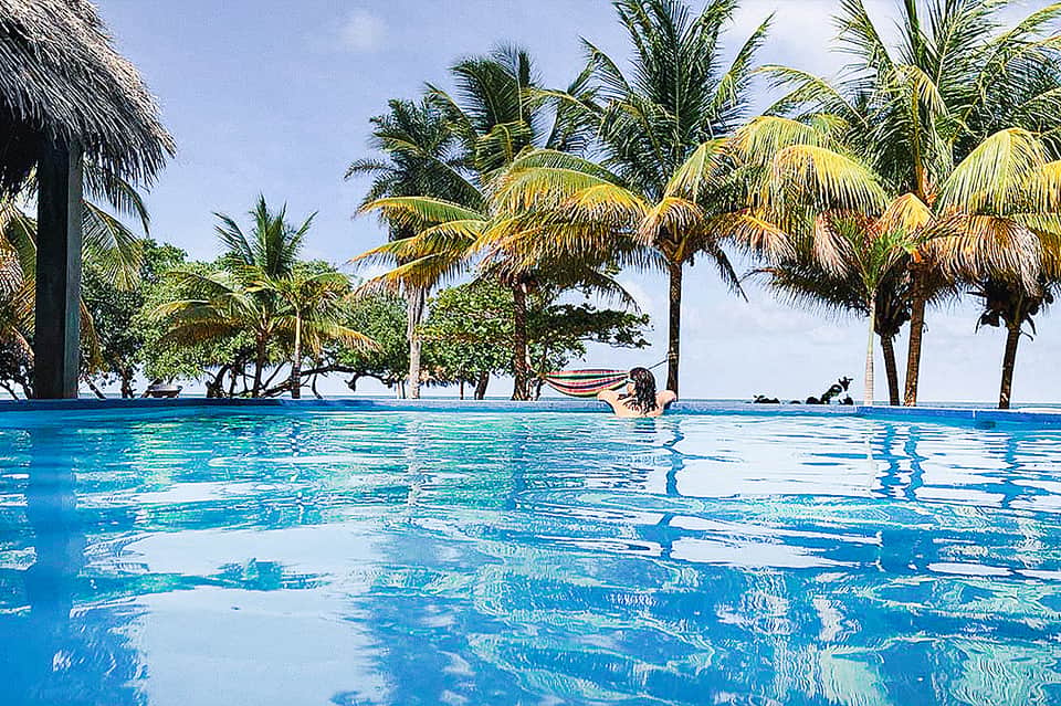 Infinity pool with palm trees reflecting in clear turquoise water with beachfront views
