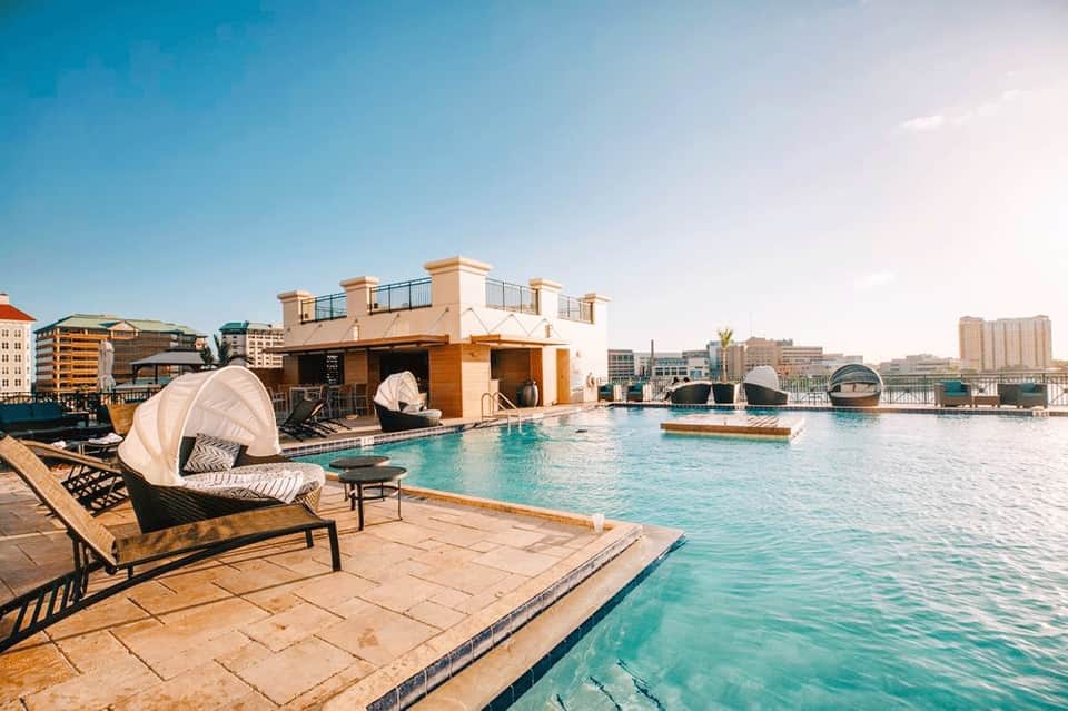 Rooftop pool deck with turquoise water, lounge seating, white cabanas, and city skyline views