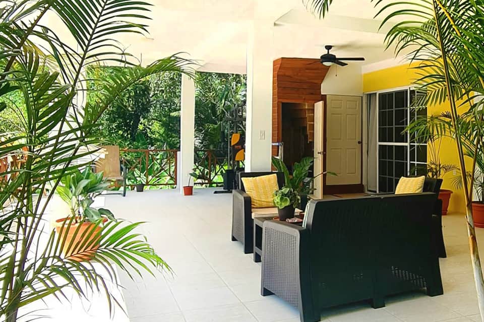 Covered outdoor patio with tropical plants, casual seating, and ceiling fan