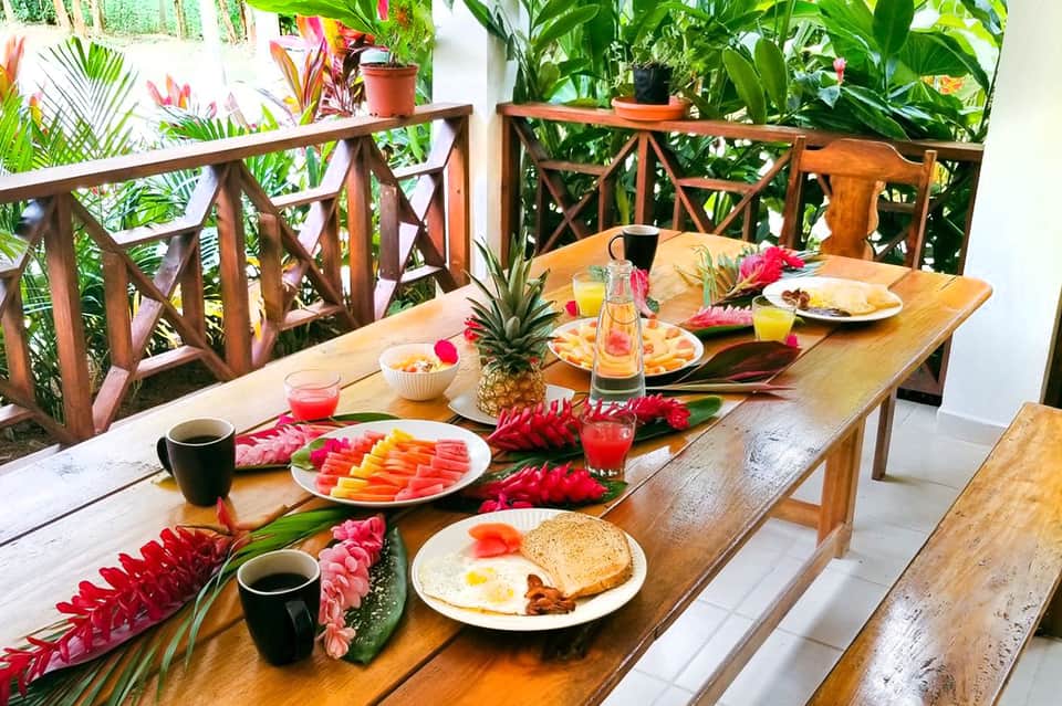 Outdoor breakfast table with tropical flowers, fresh fruit, and beachfront setting