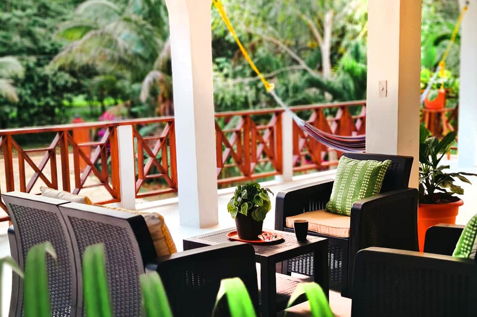 Tropical resort lounge area with black wicker furniture, green pillows, and ocean view from veranda