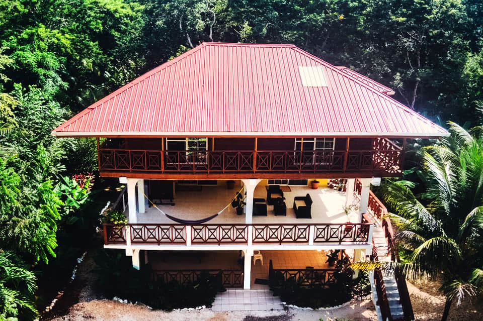 Tropical resort gazebo with red metal roof and wooden railings surrounded by lush greenery