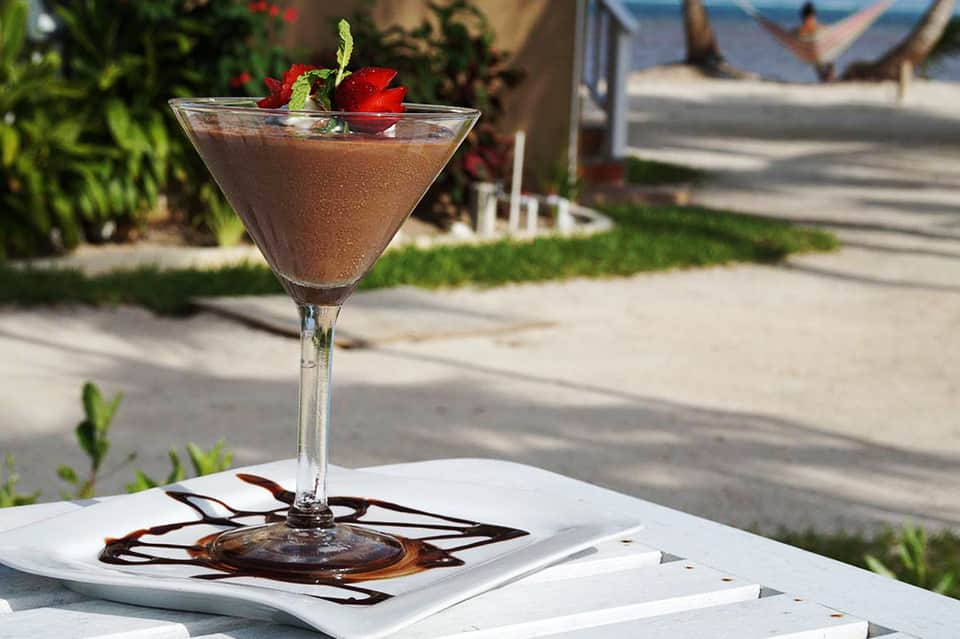 Chocolate cocktail with strawberry garnish on white plate with ocean and beach view background