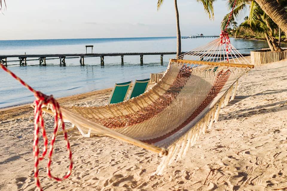 Beachfront hammock with palm trees, ocean pier, and lounge chairs