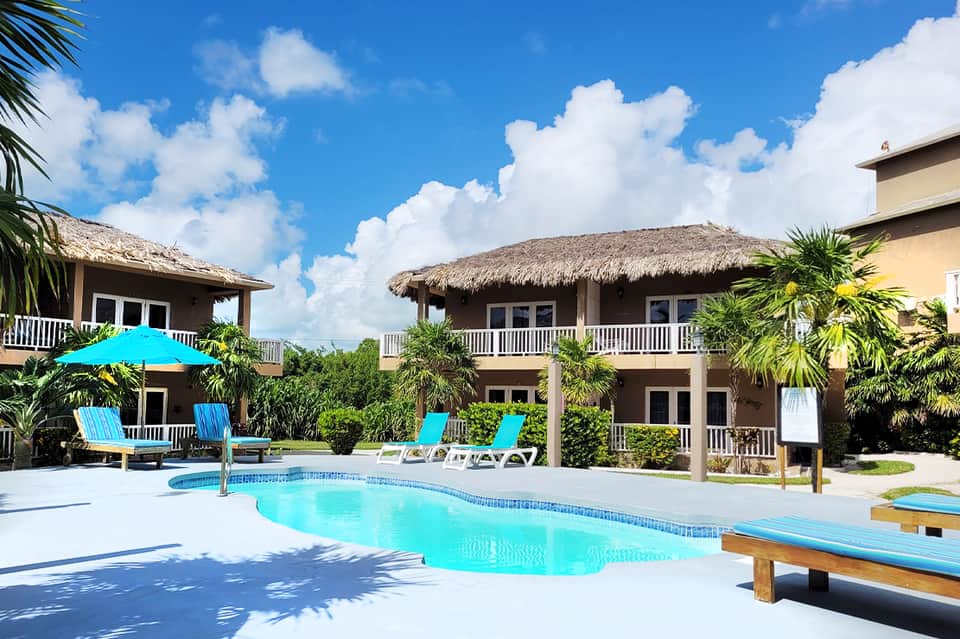 Tropical resort with thatched-roof bungalows, pool, lounge chairs, and lush landscaping