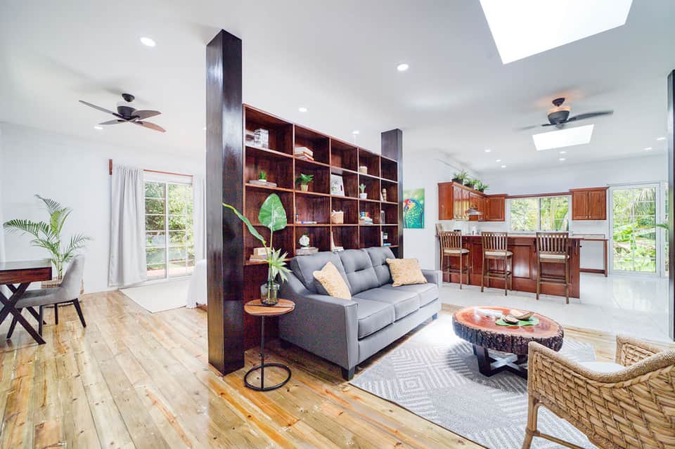 Modern resort living room with gray sofa, wooden shelving, and open kitchen area