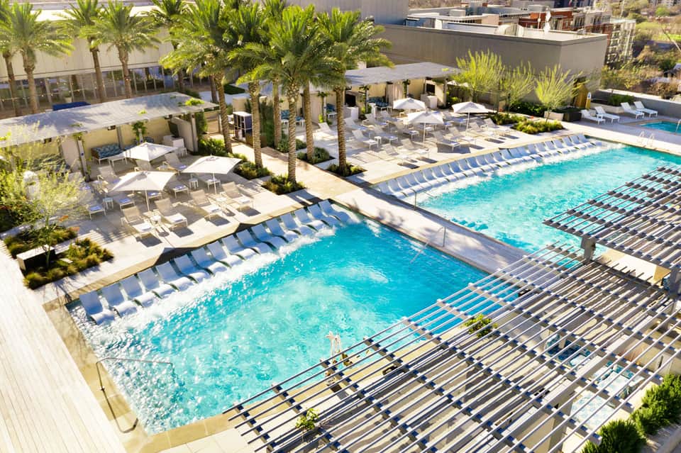 Luxurious resort pool with blue loungers, palm trees, and modern architecture overlooking city skyline