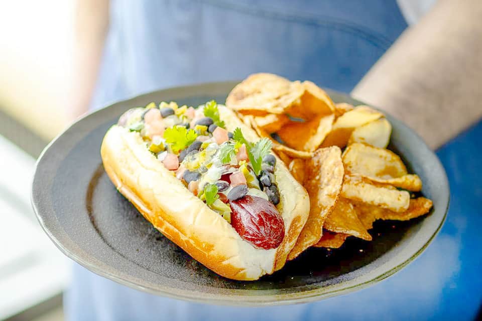 Gourmet hot dog with toppings and crispy fries on a gray plate