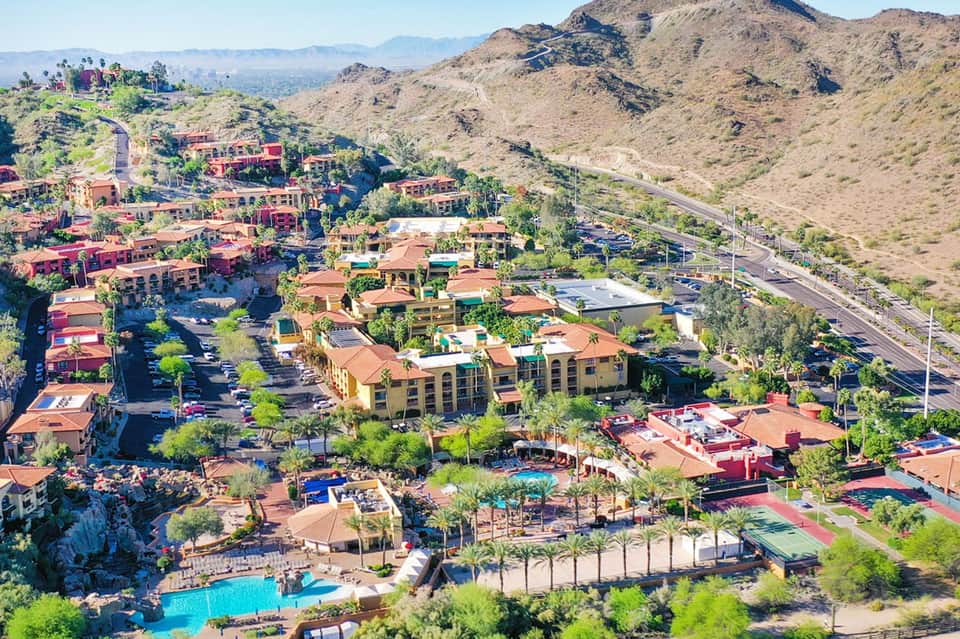 Aerial view of desert resort nestled in mountains with red-tiled buildings and pools