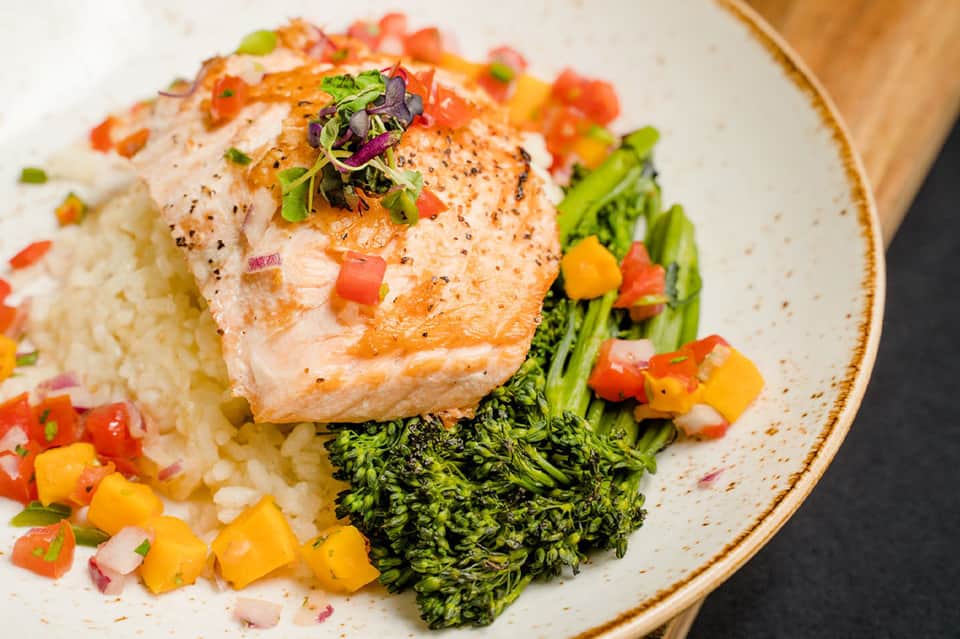 Gourmet salmon fillet with rice, broccoli, and colorful vegetable garnish on white plate