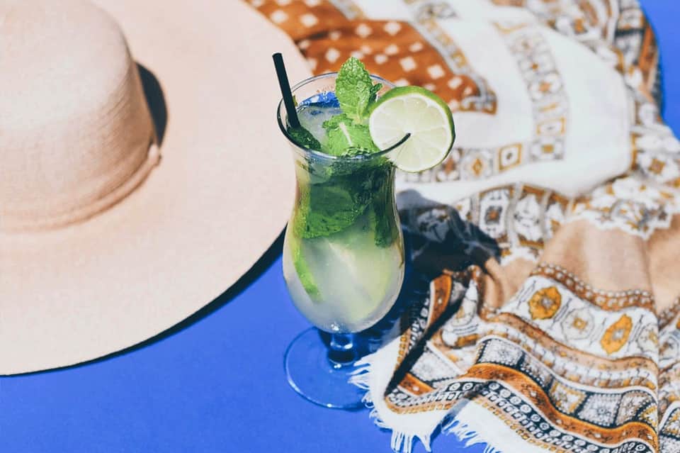 Mojito cocktail with lime slice and mint garnish on blue poolside surface with decorative towels