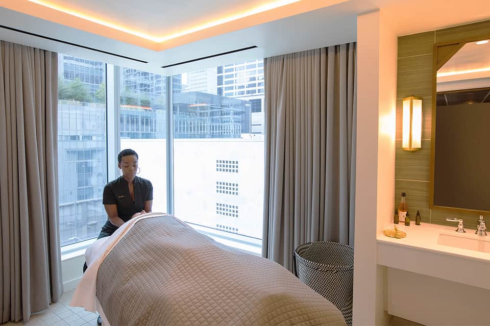 Spa therapist performing massage treatment in modern high-rise hotel room with city views