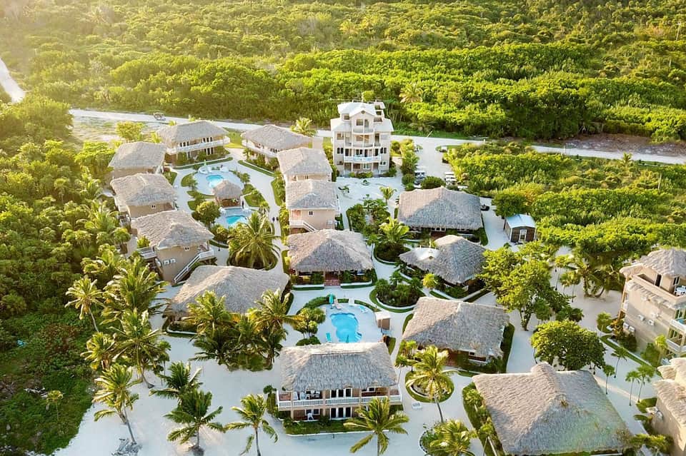 Aerial view of tropical luxury resort with thatched-roof bungalows, pools, and lush vegetation