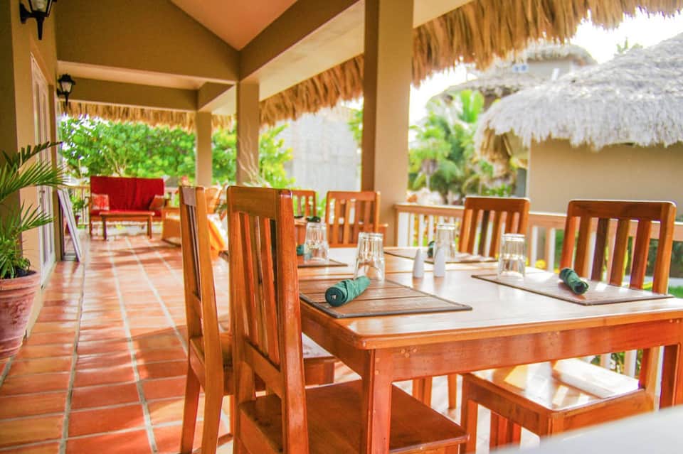 Covered dining area with wooden tables and chairs overlooking tropical gardens and ocean