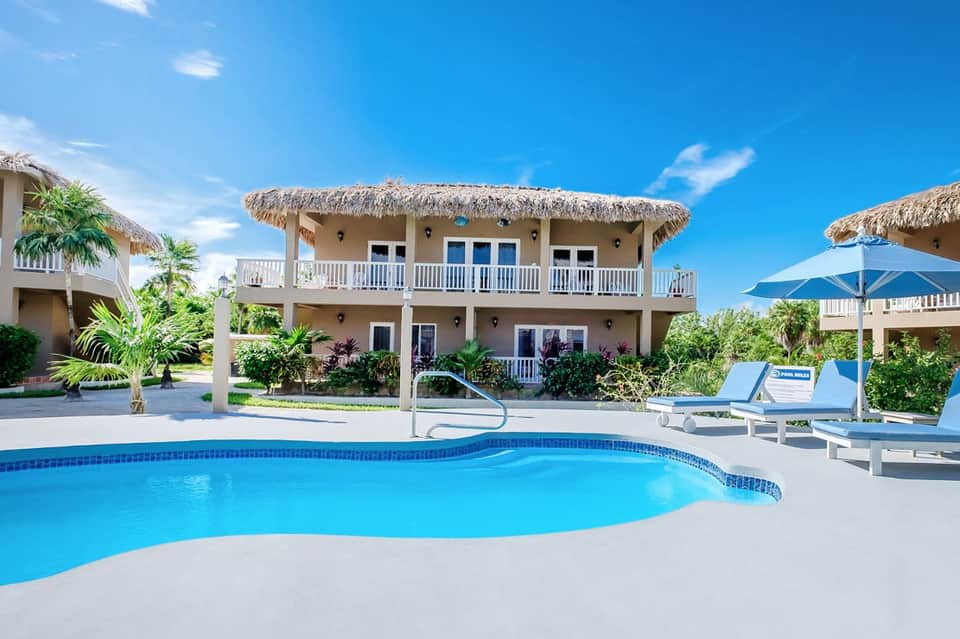 Two-story beachfront villa with thatched roof, pool, lounge chairs, and palm trees