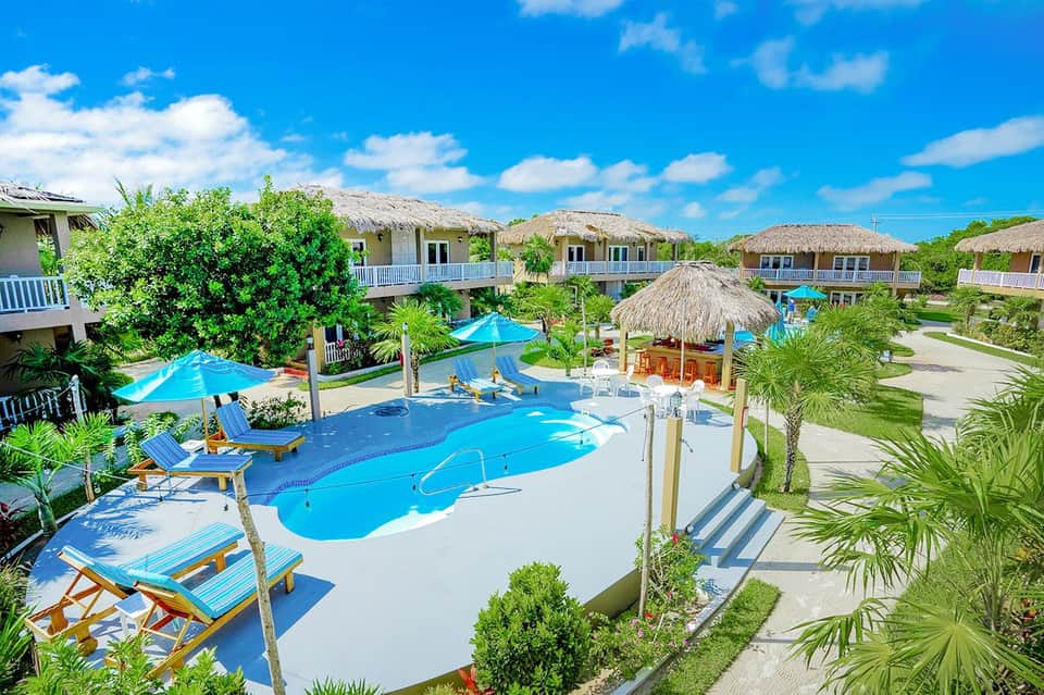 Tropical resort pool complex with thatched-roof bungalows and lounge seating areas
