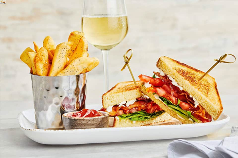 Gourmet sandwich and fries plate with white wine glass on elegant dining table