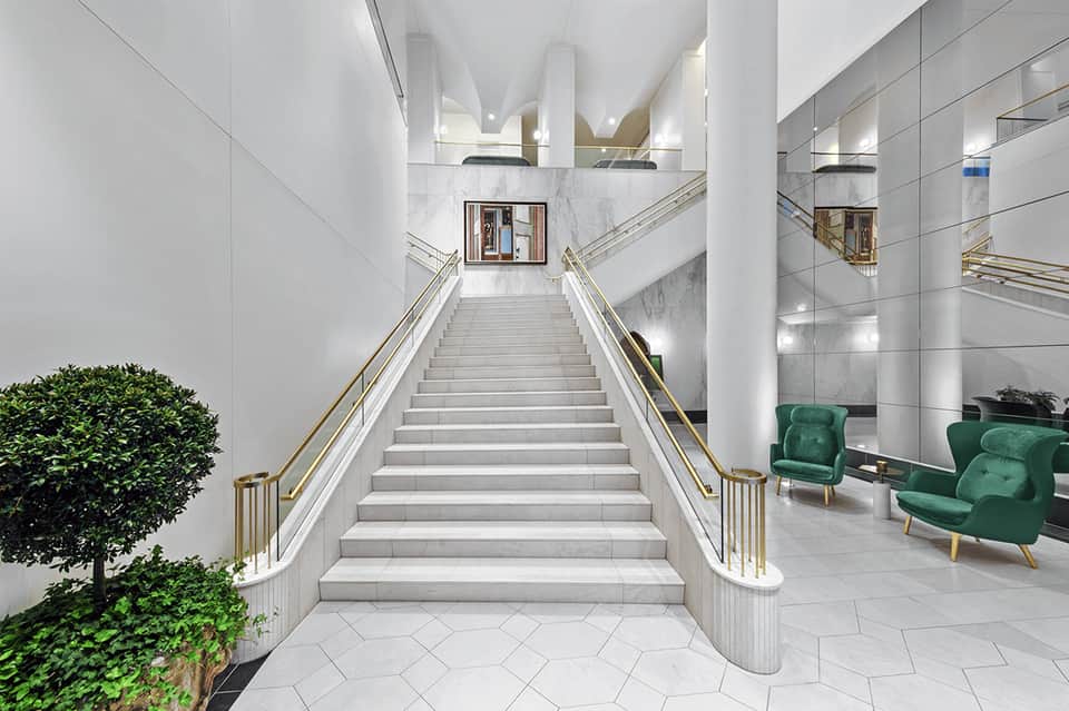 Modern white staircase with gold railings and green seating area in luxury hotel lobby