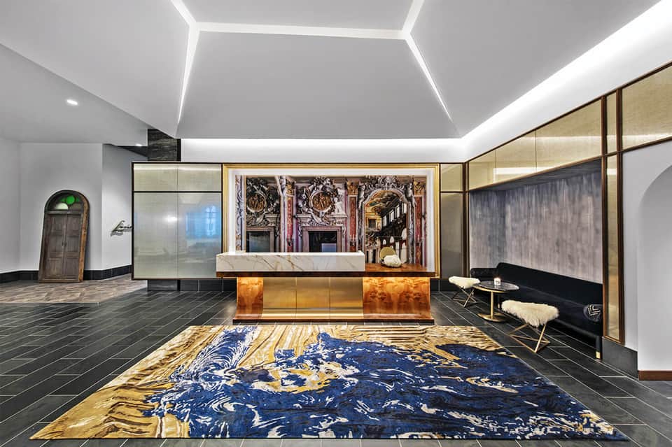 Luxury hotel lobby with marble reception desk, geometric ceiling, and decorative blue and gold rug