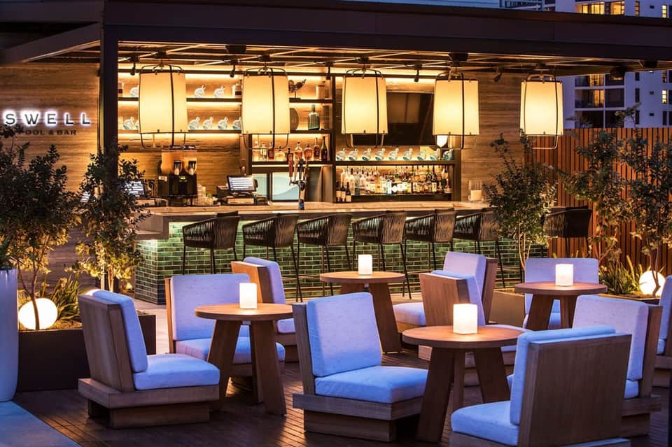 Upscale outdoor pool bar at night with illuminated signage and blue seating areas