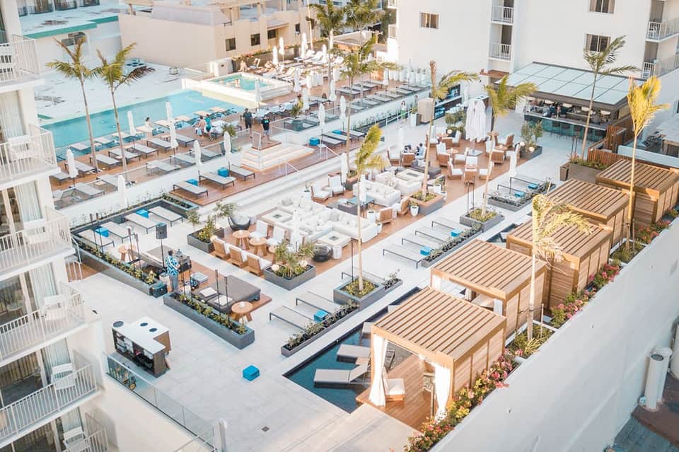 Aerial view of resort pool deck with white loungers, umbrellas, cabanas, and turquoise pools surrounded by palm trees