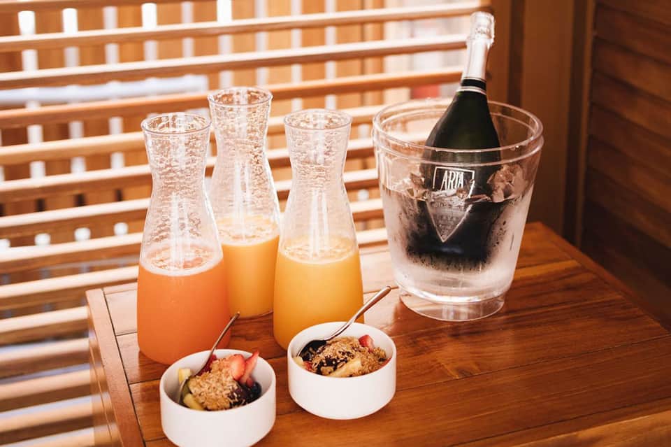 Champagne bottle in ice bucket with juice glasses and breakfast bowls on wooden table