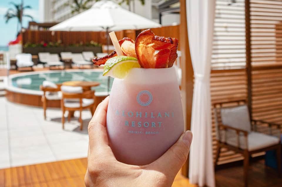 Tropical cocktail with fruit garnish held at resort poolside with lounge chairs visible