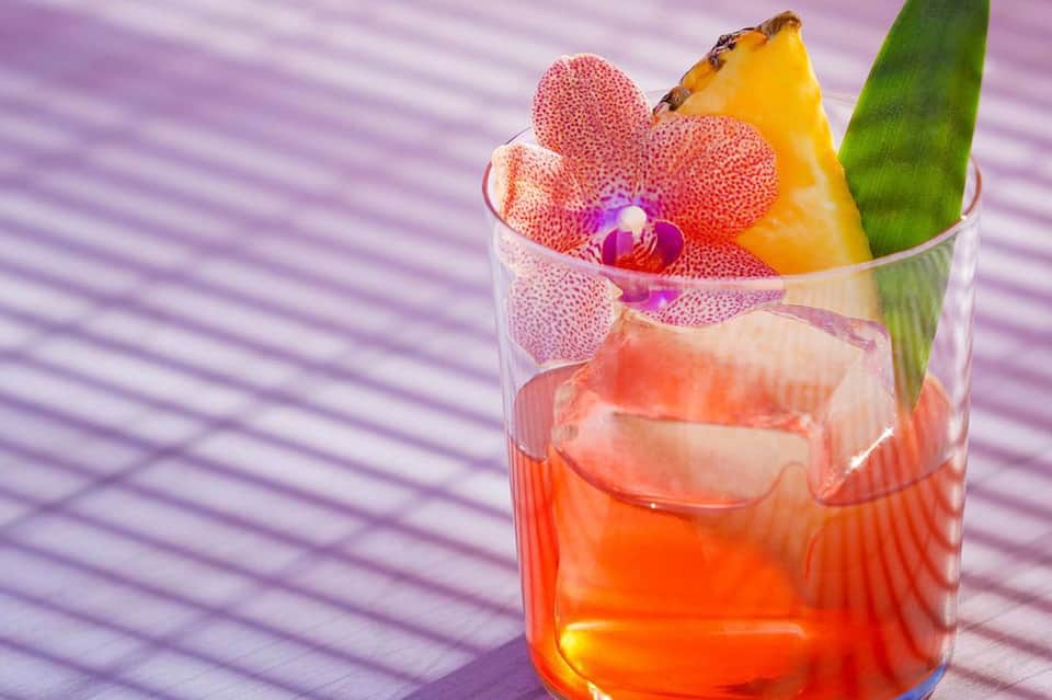 Tropical cocktail with orchid flower and mango garnish on purple striped surface