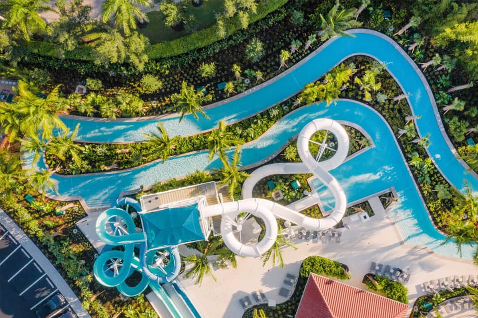 Aerial view of turquoise lazy river winding through lush tropical gardens with white structures
