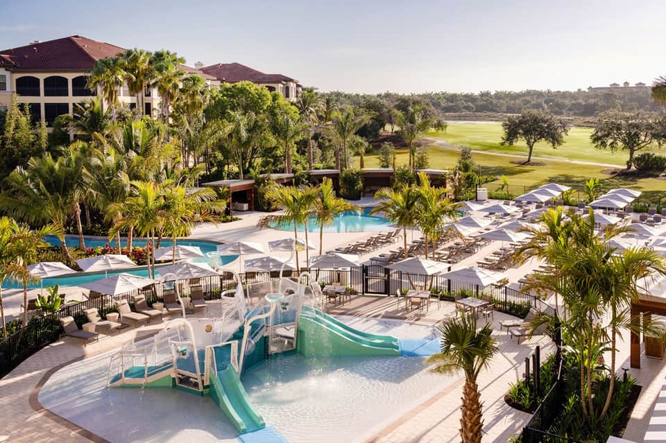 Luxury resort pool complex with waterslide, multiple pools, palm trees, and golf course views