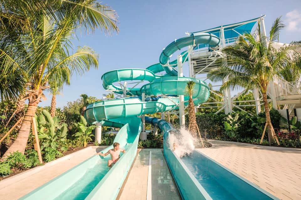 Family enjoying turquoise water slides at tropical resort surrounded by palm trees