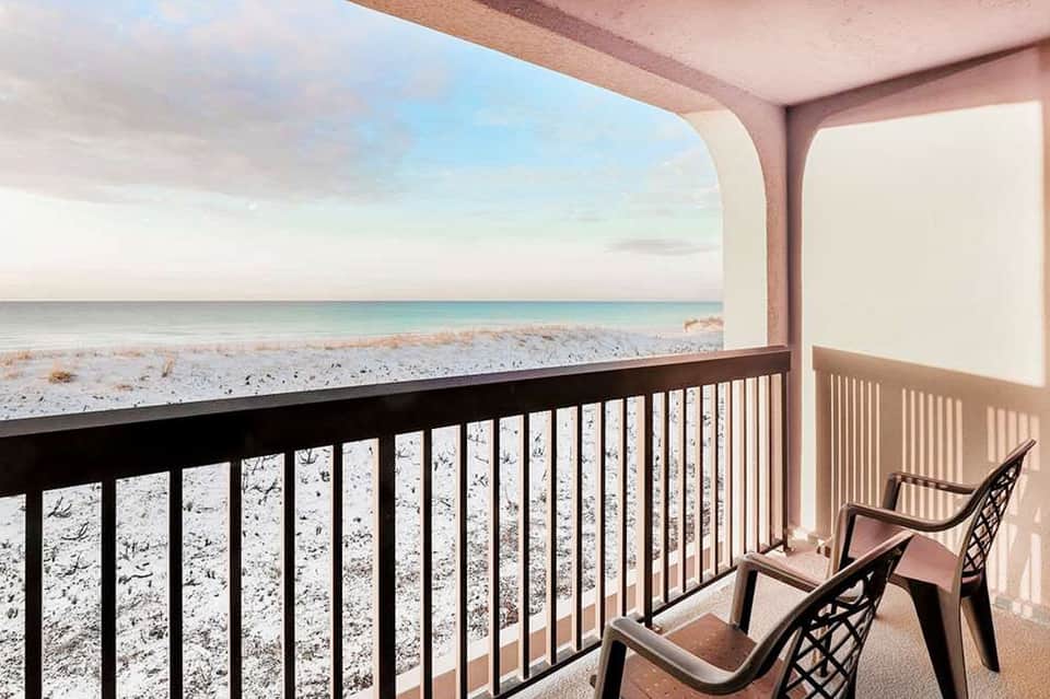 Beachfront balcony with ocean view, white railing, and two lounge chairs at sunset