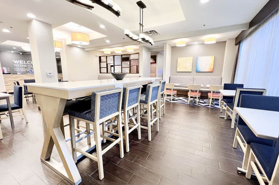 Modern hotel bar and lounge area with high-top seating, blue cushioned chairs, and contemporary lighting