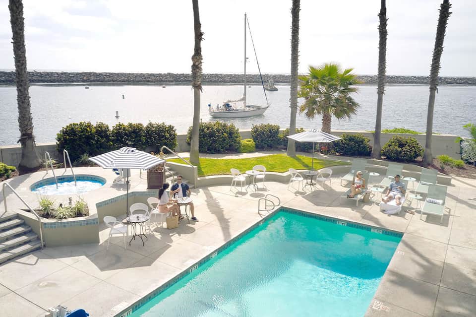 Waterfront resort pool area with palm trees, sailboat visible on bay, and lounging guests