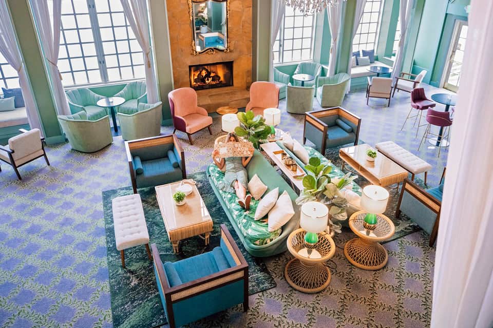 Modern hotel lounge with fireplace, colorful mid-century furniture, windows, and decorative elements