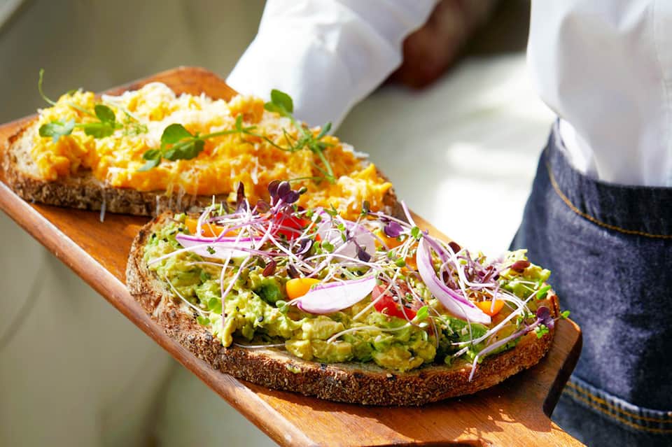Gourmet open-faced sandwiches with avocado and microgreens on wooden serving board