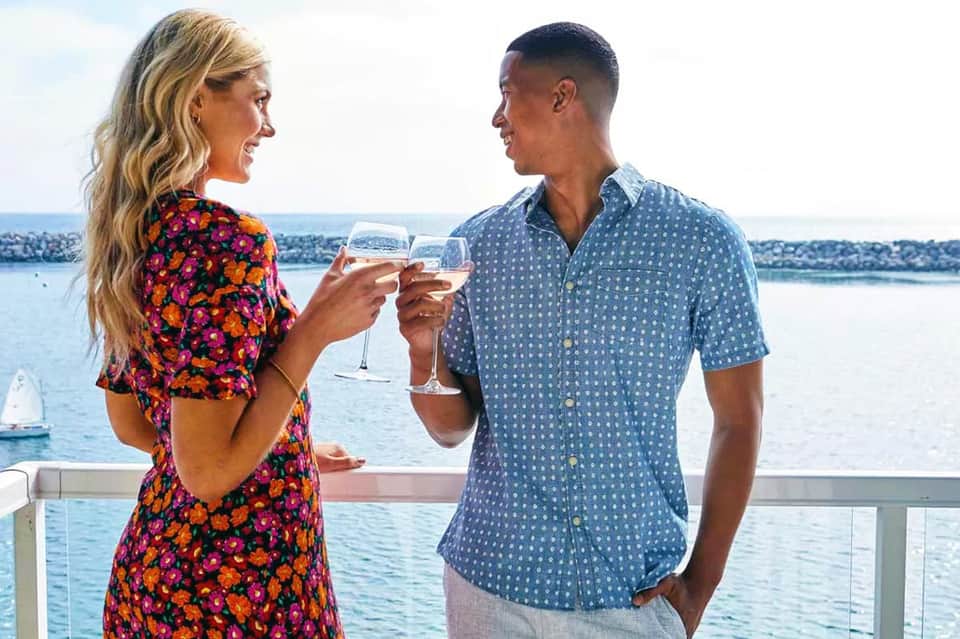 Couple toasting with wine glasses on a balcony overlooking a waterfront with sailboats