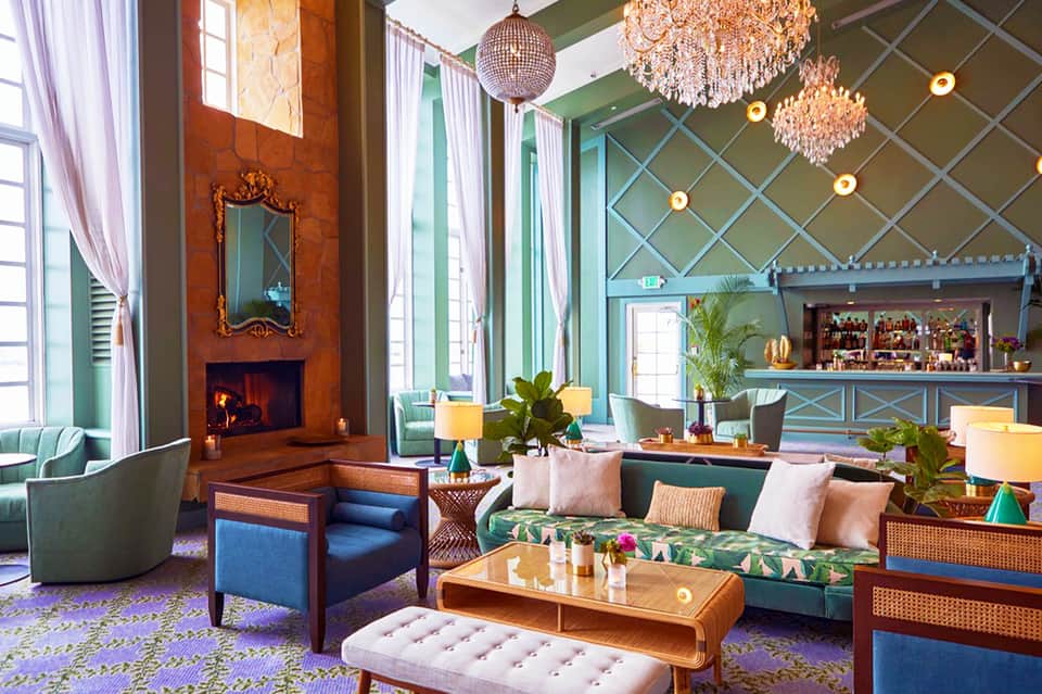 Luxury hotel lounge with fireplace, chandeliers, green walls, colorful seating, and botanical accents